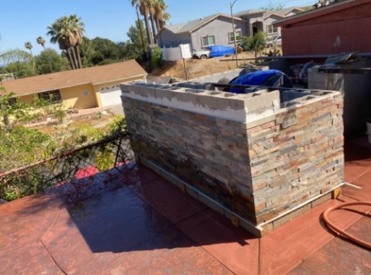 Outdoor rooftop patio with a stone fire pit, red concrete floor, and blue chairs in a desert neighborhood