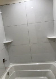 White tiled shower or bathtub area with corner shelves and a faucet