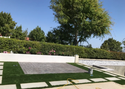 Landscaped garden with white walls, green hedges, a tree, and a paved ramp under a blue sky