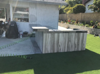 Backyard patio with a striped outdoor kitchen island, grass lawn, and house wall in the background
