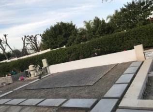 Residential rooftop with large solar panels, white parapet walls, and trees in the background