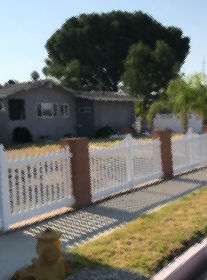 Suburban house with a white fence, large tree, and yellow fire hydrant by the curb