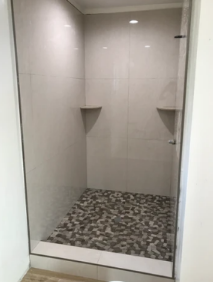 Empty tiled shower stall with pebble floor and built-in corner shelves