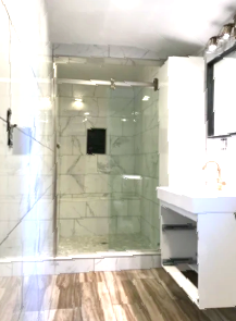 Small bathroom with glass shower enclosure, white sink, and wood-look floor.