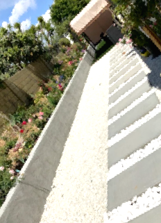 Sunlit white staircase beside a garden with pink flowers and a brick wall
