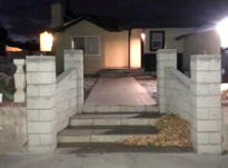 House entrance at night with a concrete staircase, brick pillars, and a lit porch in the background