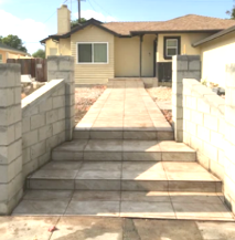 Front steps and tiled walkway leading to a beige house with a front porch and low cinderblock walls.