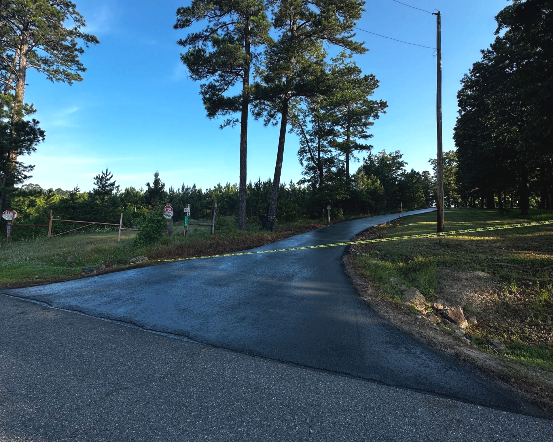 Asphalt road splitting into two paths, flanked by trees and greenery under a blue sky.