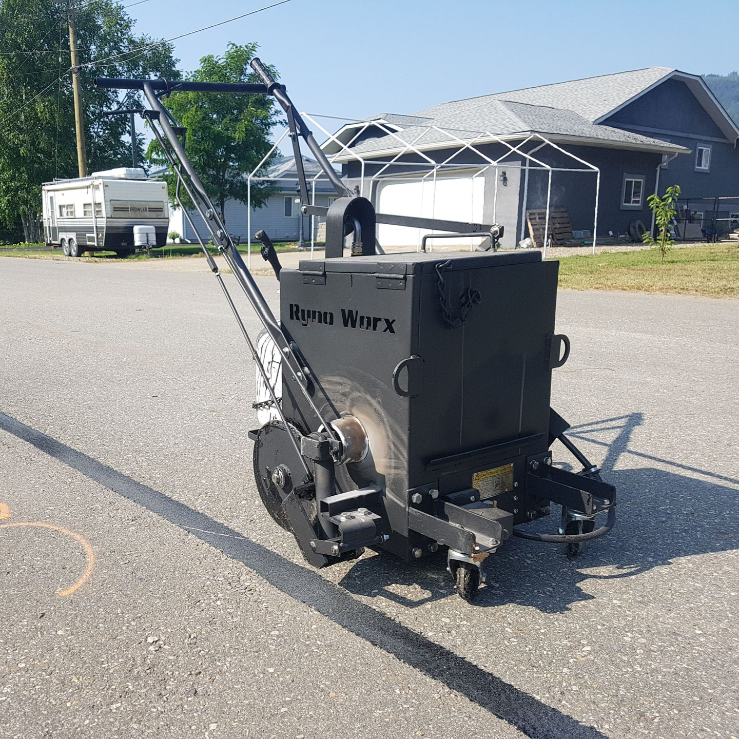 Black line painting machine applying a fresh stripe on a paved surface. Sunny outdoor setting.