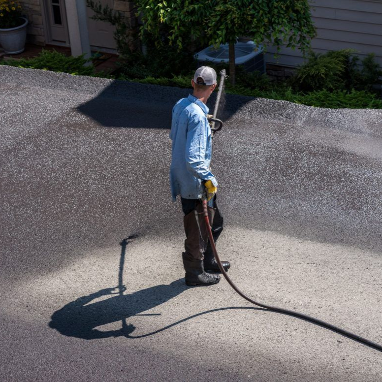Person applying coal tar sealer to residential driveway via spray application