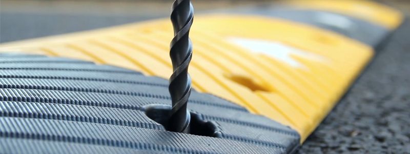 Close-up of a screw fixing a speed bump to the asphalt road. The bump is yellow and black.