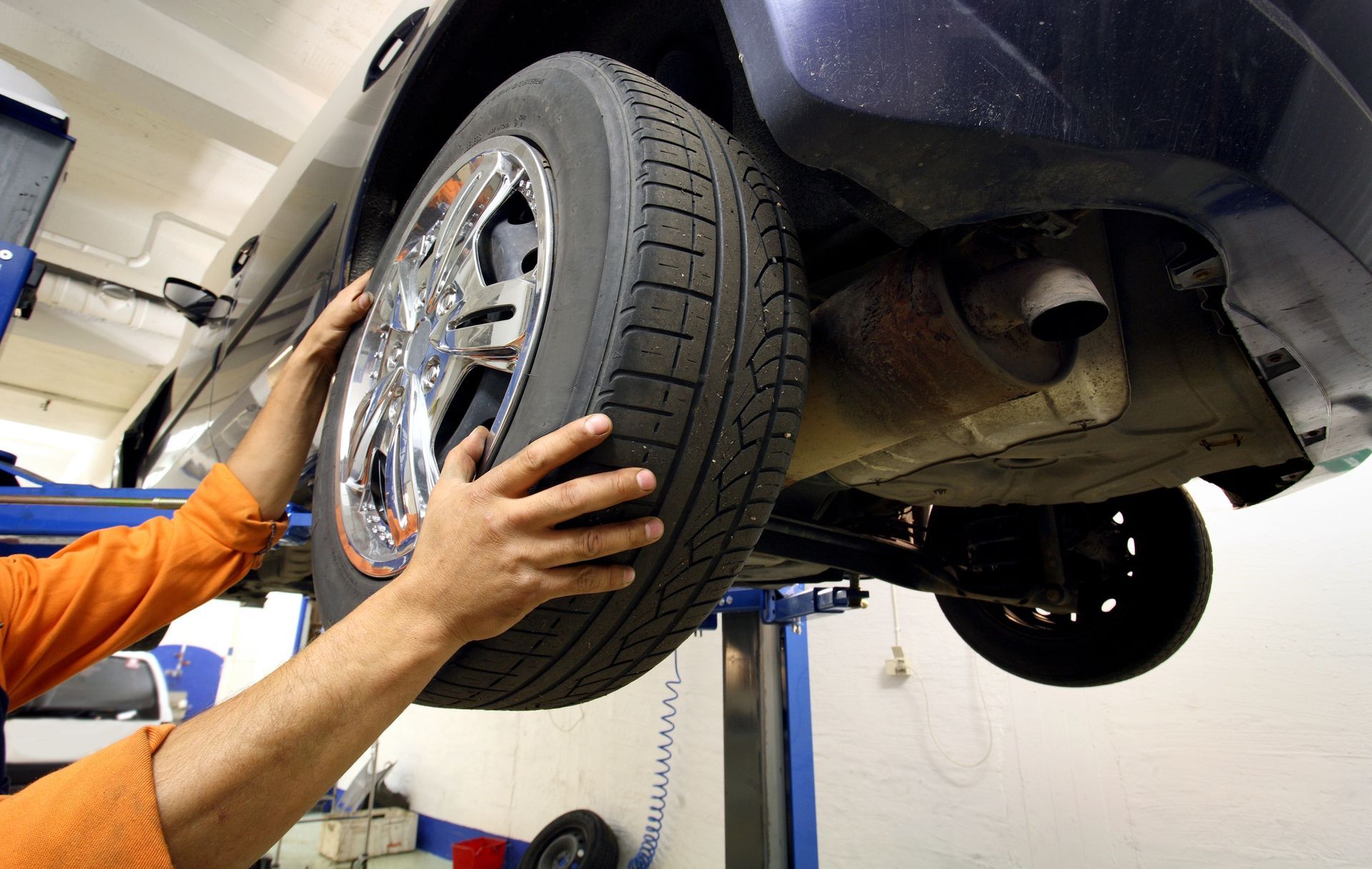 Mani che tengono uno pneumatico per auto. Auto su un ponte sollevatore in un'officina.