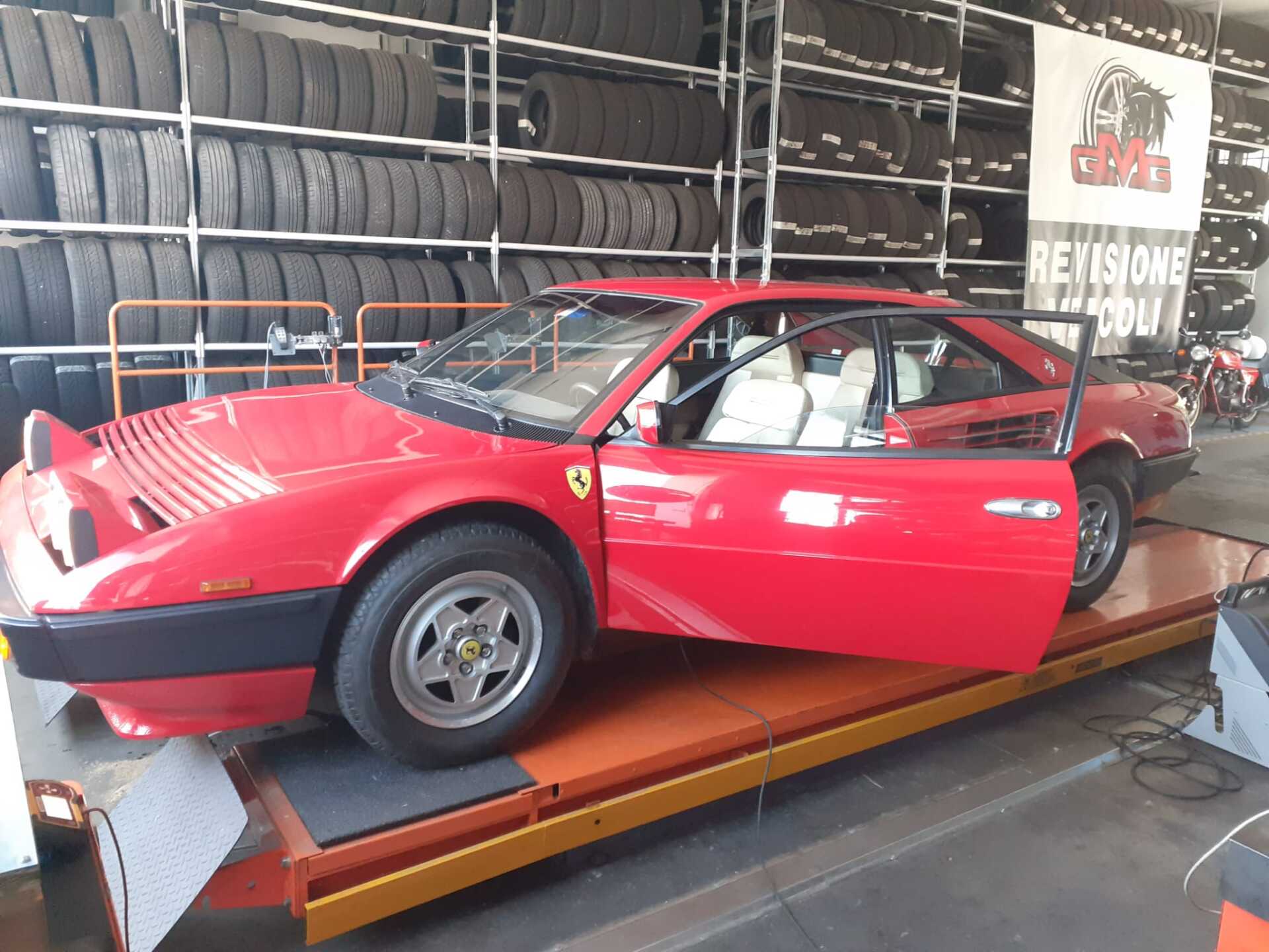 Ferrari Mondial rossa con la portiera aperta su un ponte sollevatore arancione in un gommista.