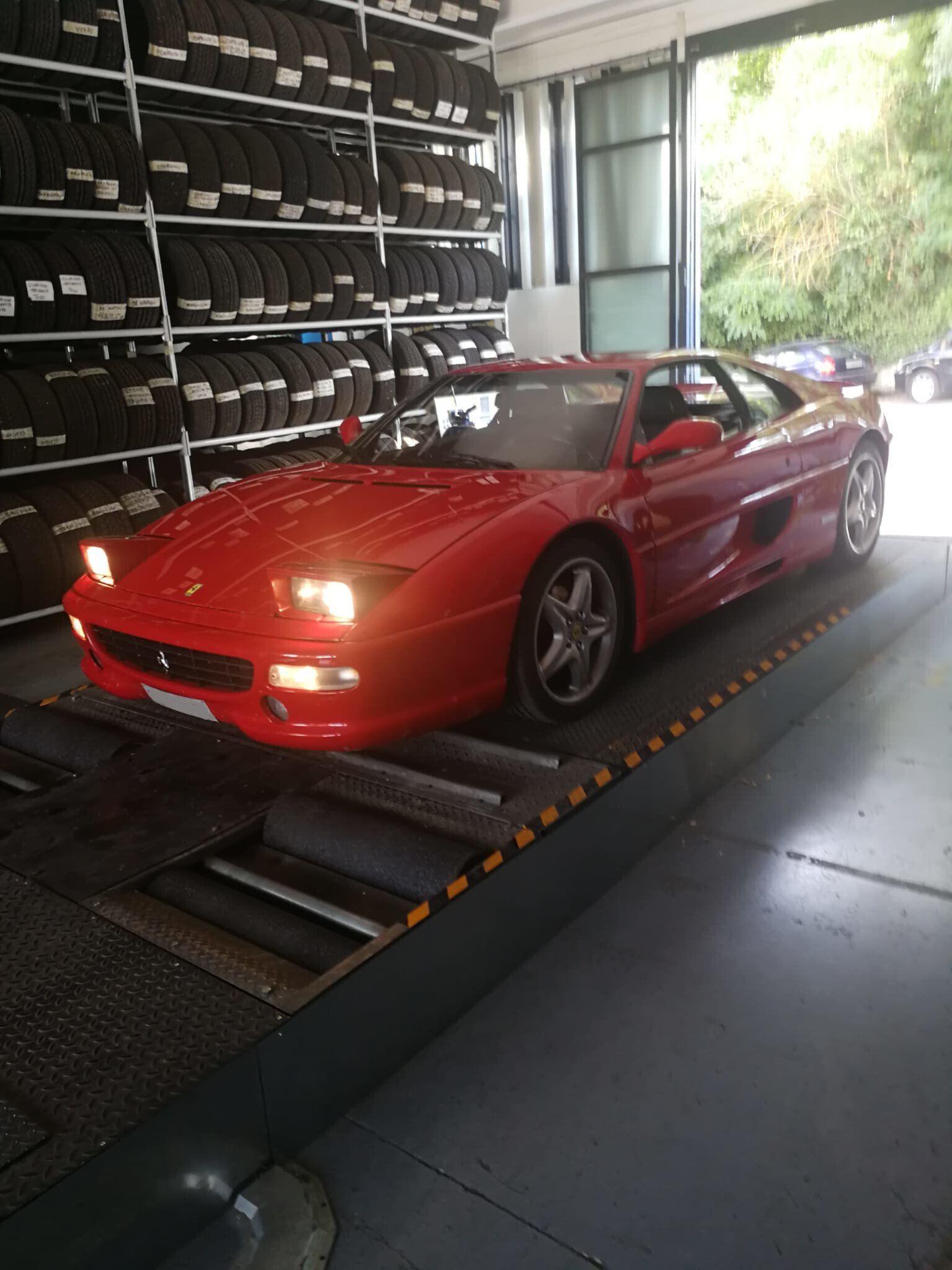 Un'auto sportiva Ferrari rossa all'interno di un garage. Sullo sfondo, pneumatici impilati.