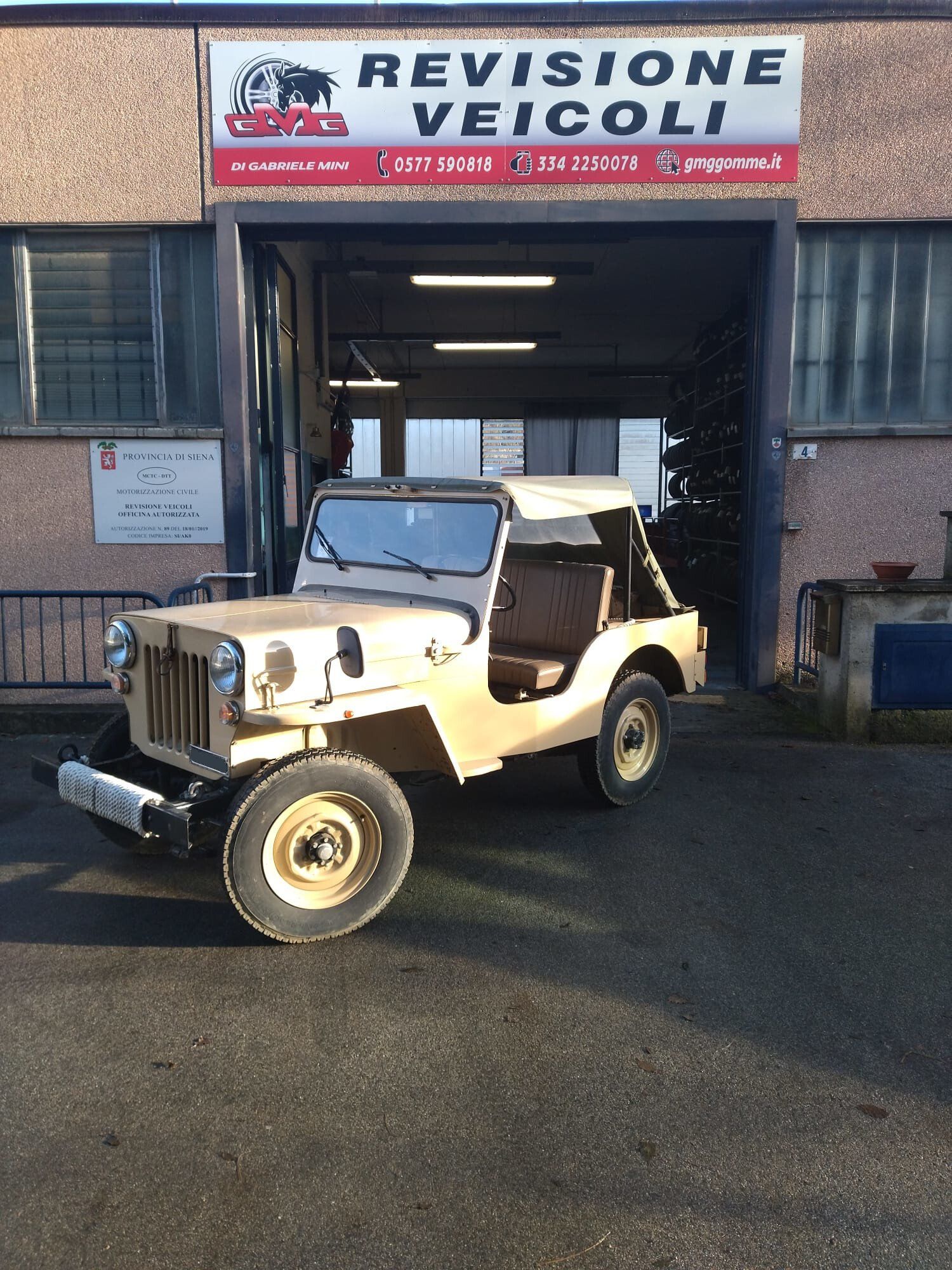 Jeep beige d'epoca parcheggiata davanti a un'officina con il cartello 