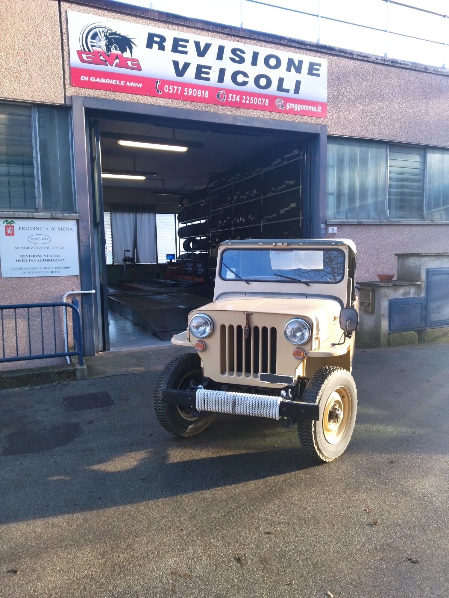 Jeep d'epoca color marrone parcheggiata davanti a un'officina di revisione veicoli.
