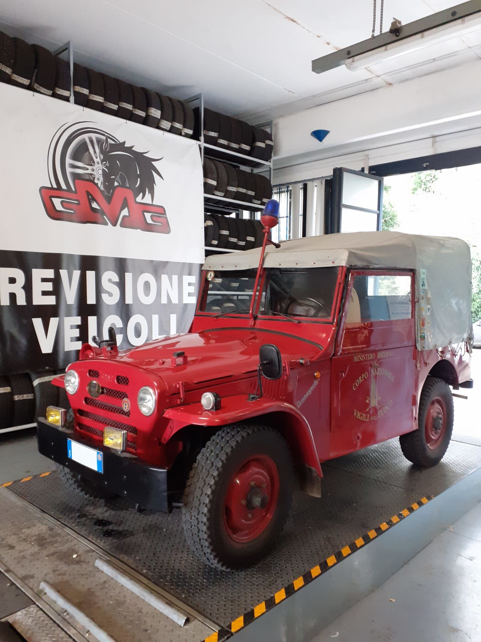 Veicolo fuoristrada d'epoca rosso all'interno di un garage. Ha un tetto in tela e una luce blu e rossa sulla parte superiore.