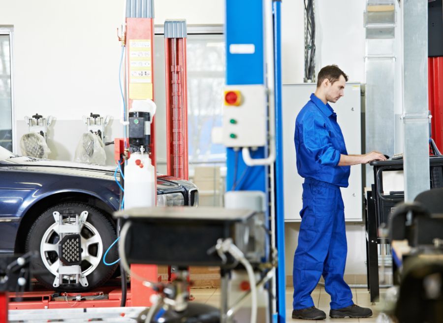 Meccanico in tuta blu che utilizza una macchina per allineare una ruota di un'auto in un'officina.