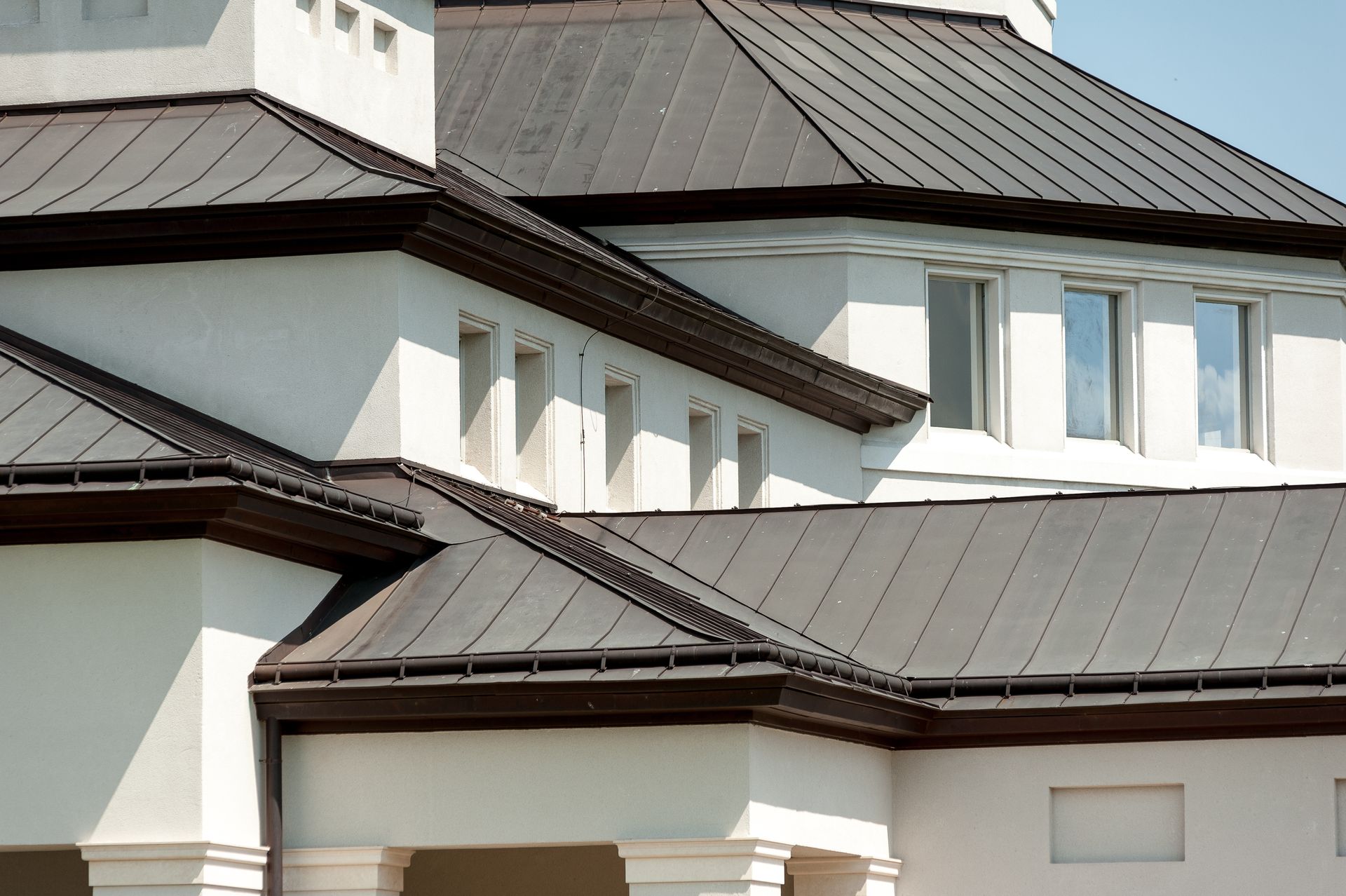 White building with dark gray metal roof, brown trim, and small windows.
