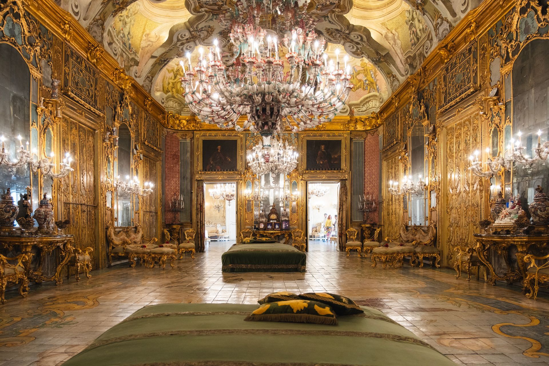 Sala da ballo sfarzosa e dorata con lampadari di cristallo, specchi e pavimento in marmo lucido.