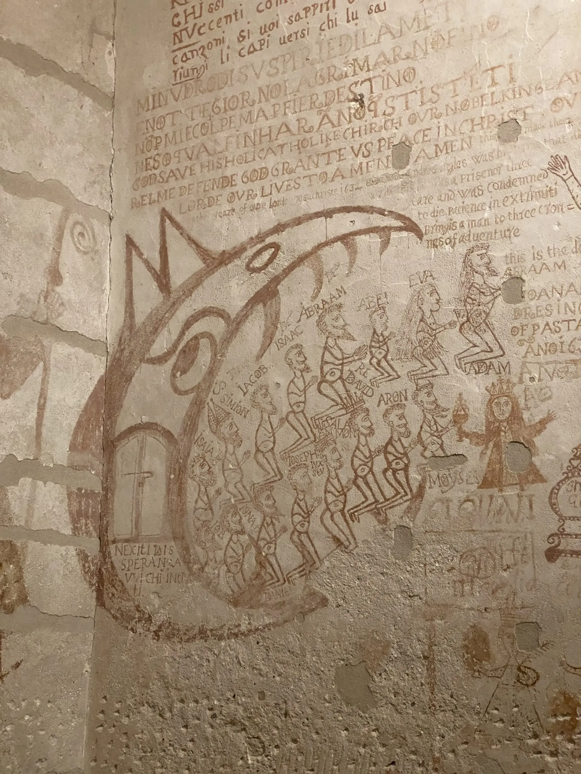 Murale sbiadito raffigurante un grande pesce o una balena su un muro di pietra consumato dal tempo, con deboli graffiti scritti a mano.