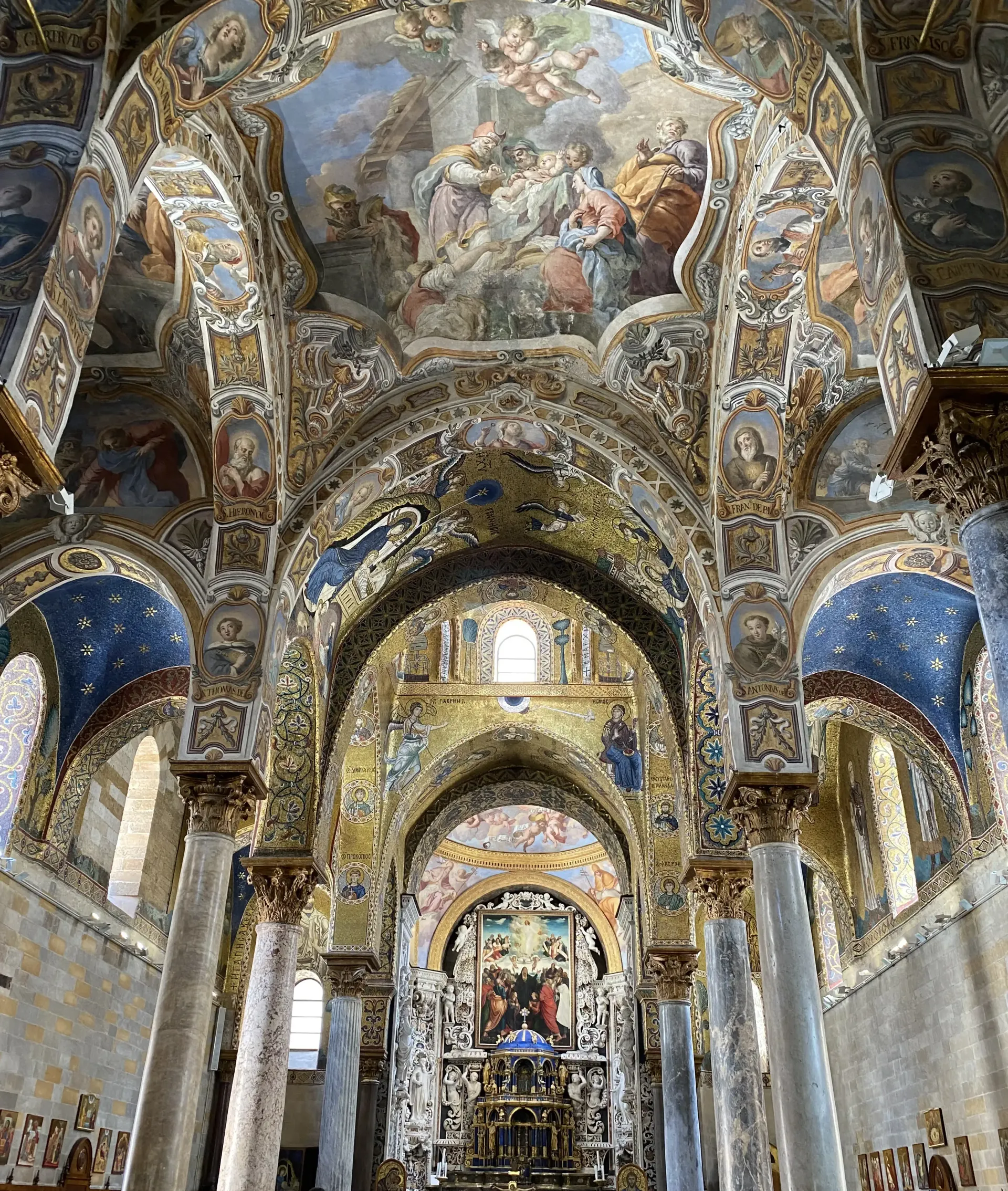 Interno della chiesa riccamente decorato con mosaici dorati, soffitto a volta e altare centrale sotto affreschi.