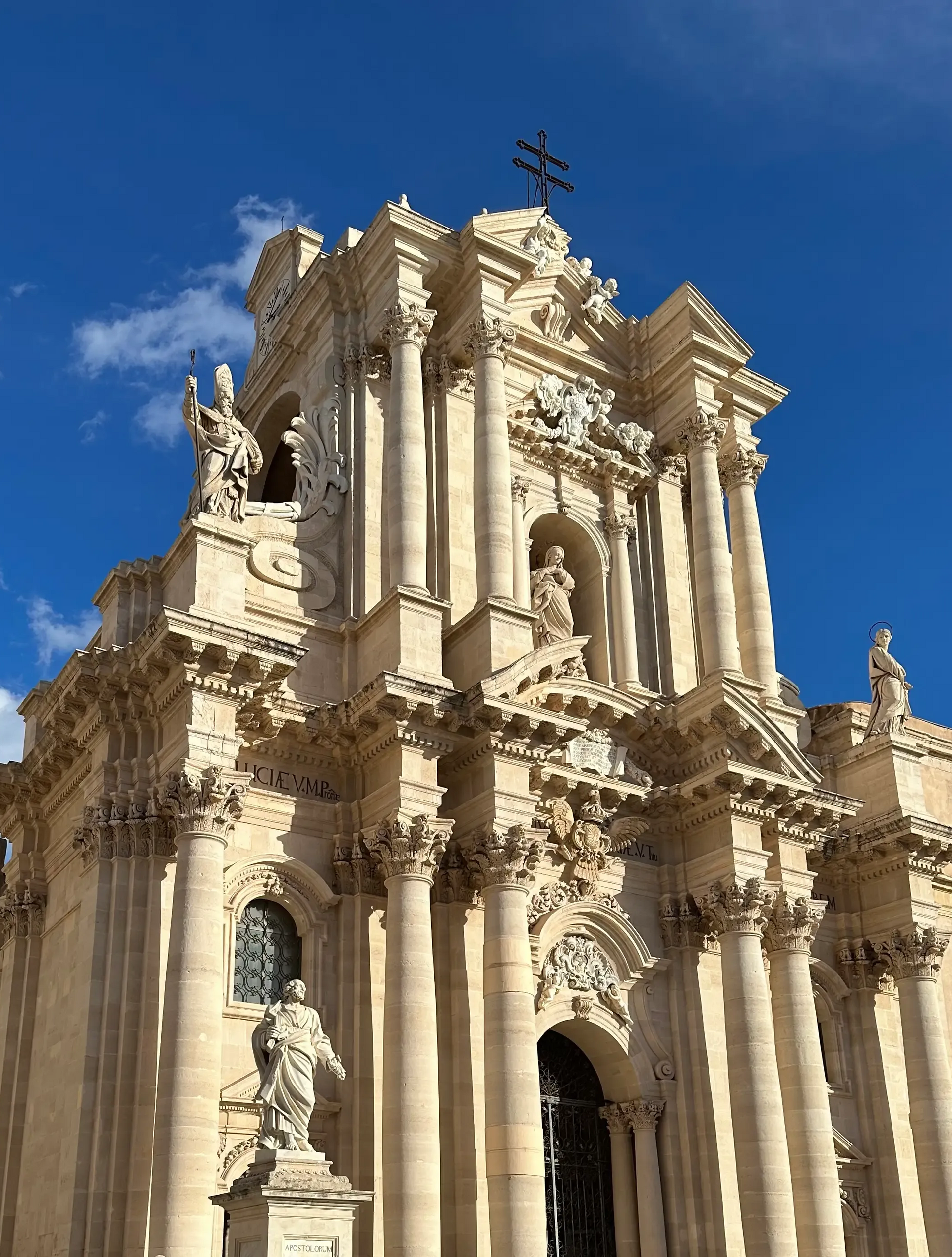 Facciata di cattedrale in pietra riccamente decorata con alte colonne e statue stagliate contro un cielo azzurro brillante.