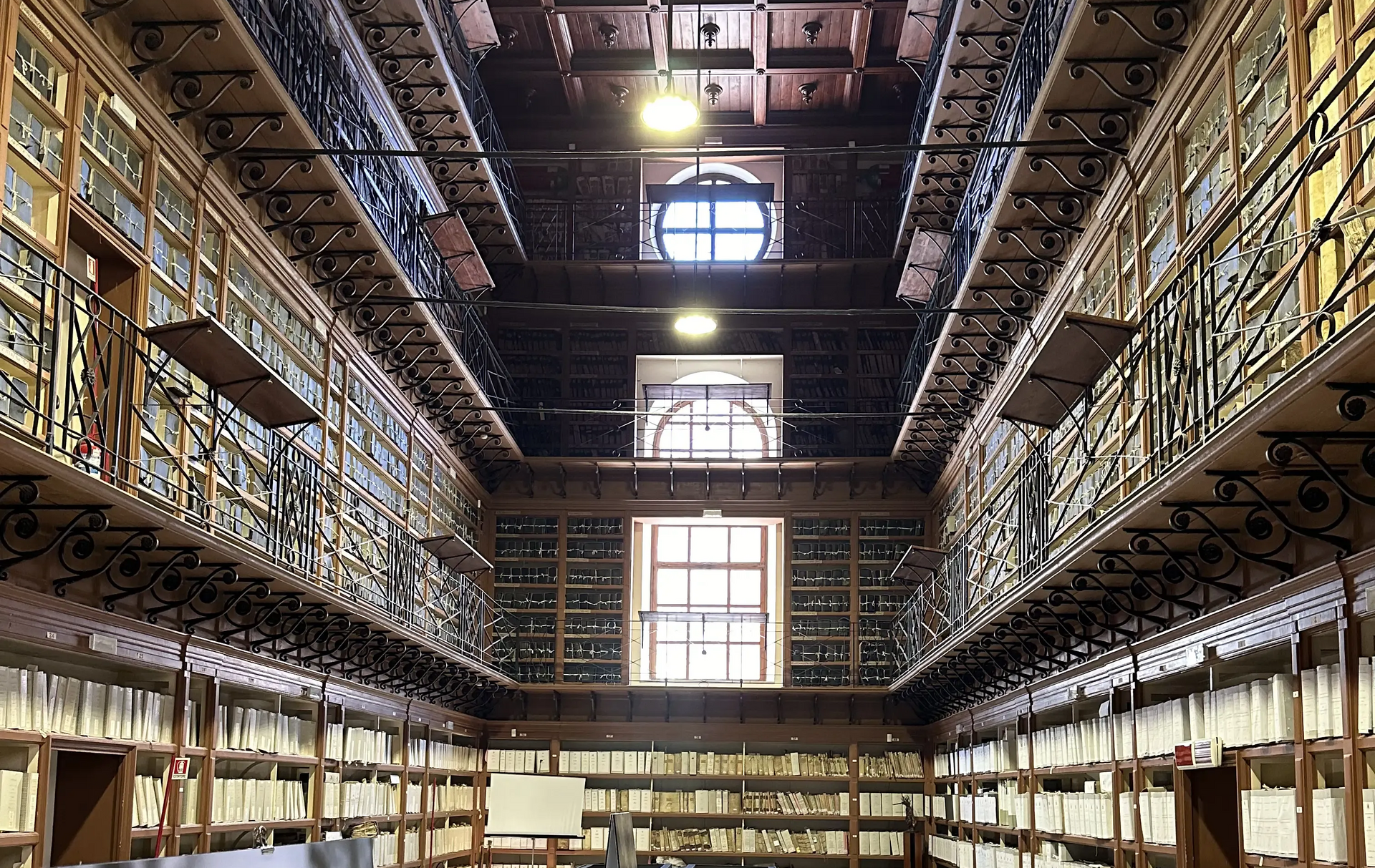 Ampio interno della biblioteca con alte librerie, balconi decorati e un grande lucernario sul soffitto.