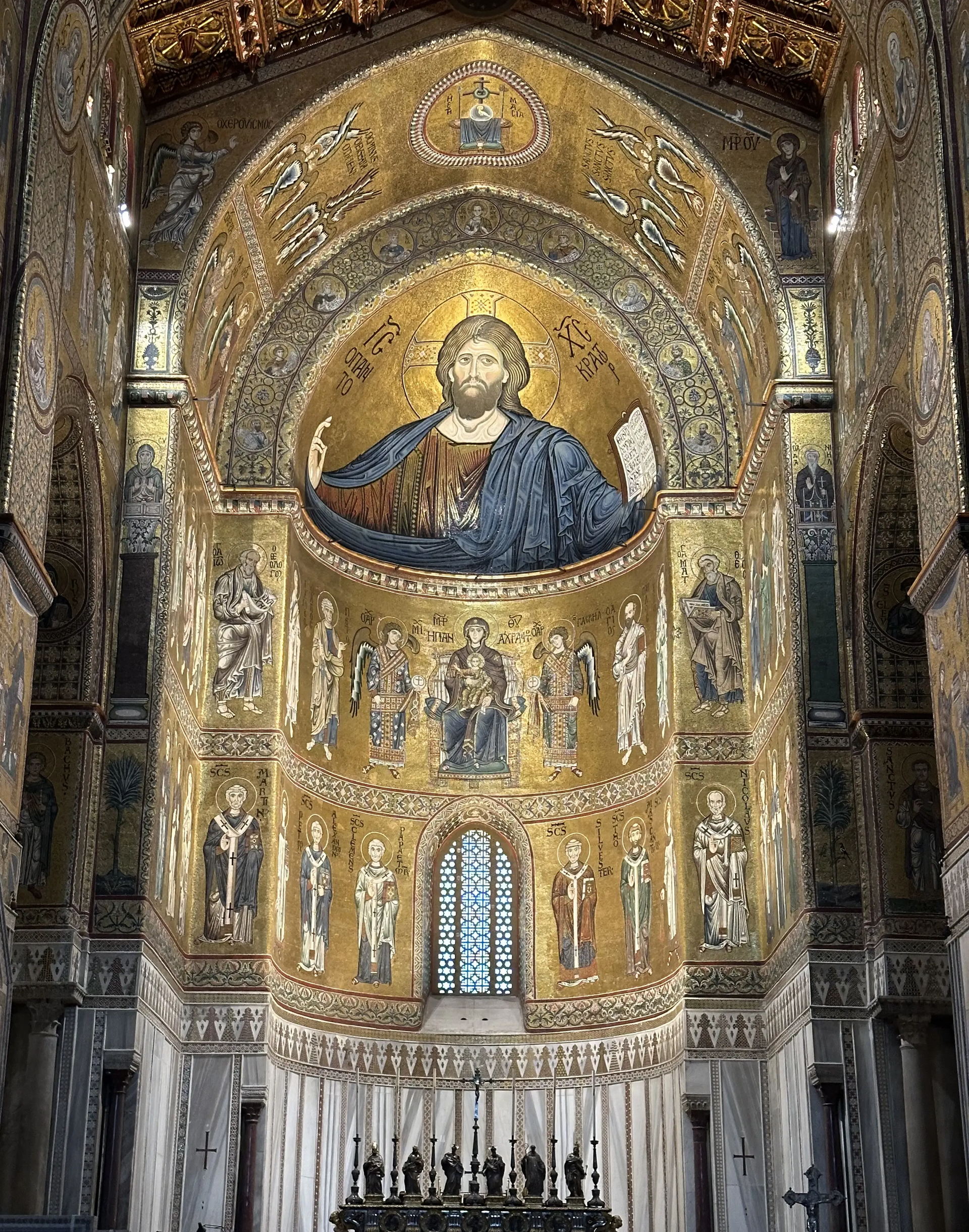 Mosaico dorato di Cristo sopra un altare e un'abside di una chiesa riccamente decorati, con pareti ad arco e candelabro.