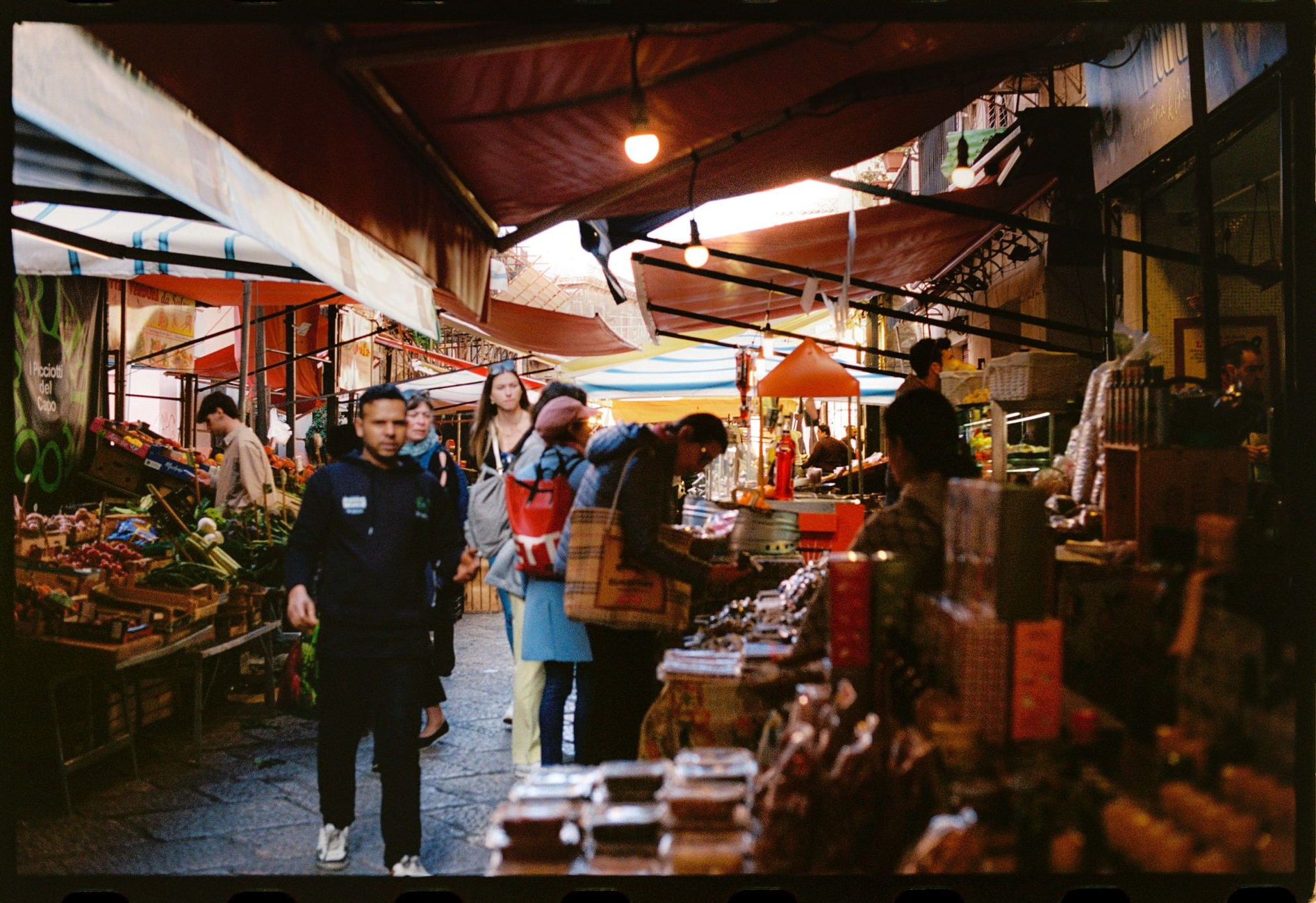 Un vivace mercato coperto con acquirenti sotto tendoni rossi e merci accatastate sulle bancarelle.