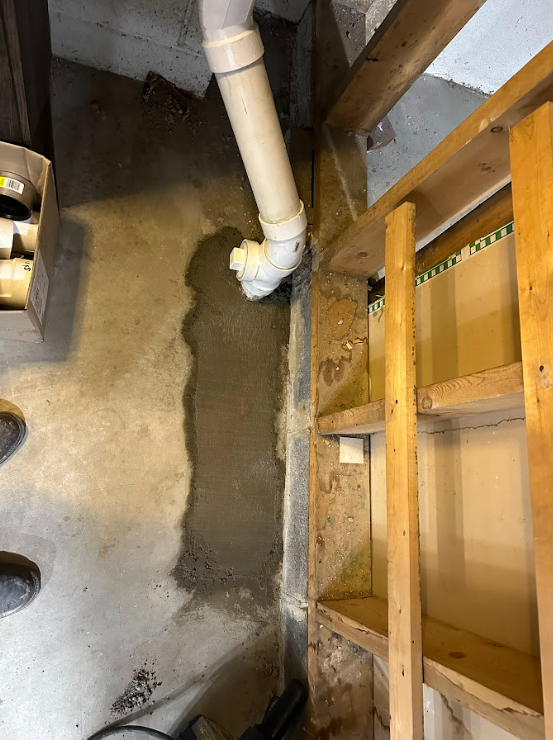A person is standing next to a pipe in a basement.