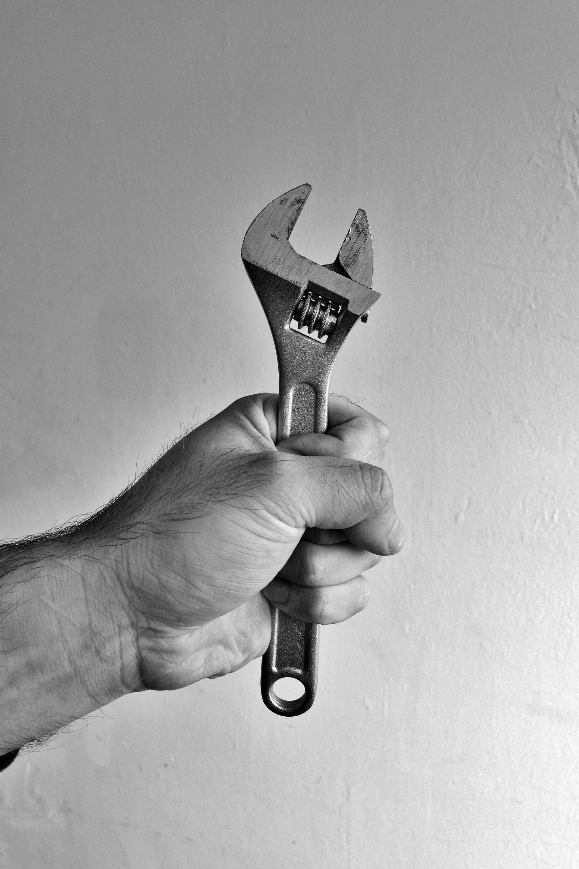 A person is holding a wrench in their hand in a black and white photo.