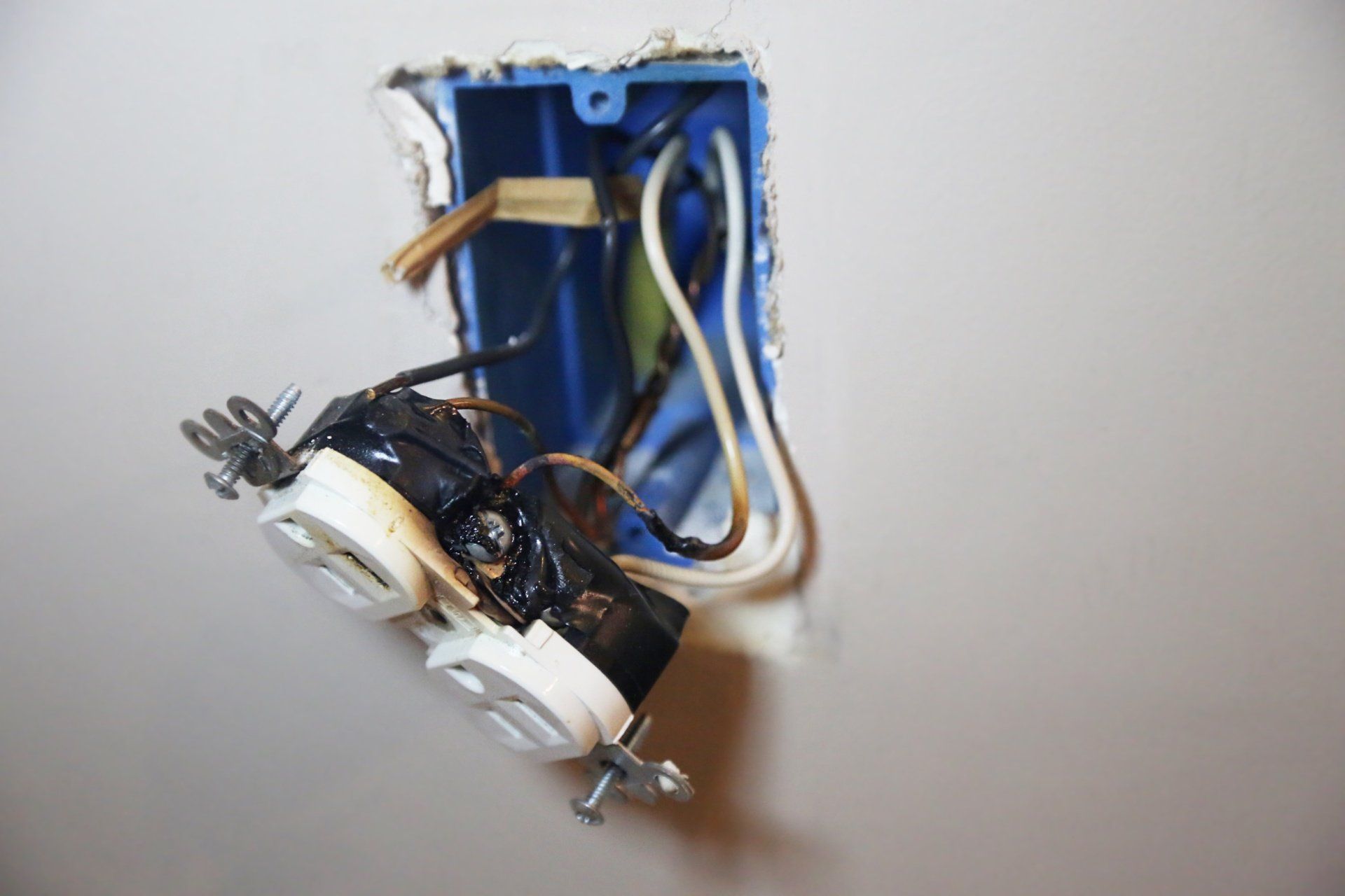 A broken electrical outlet on a wall with wires coming out of it.