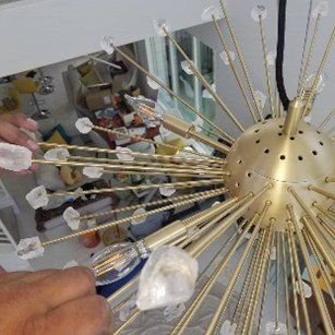 A person is fixing a chandelier with a screwdriver.