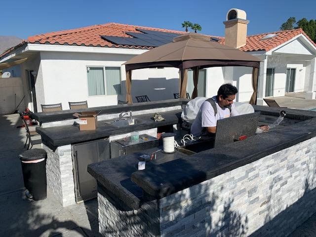 A man is sitting at a table with a laptop in front of a house.