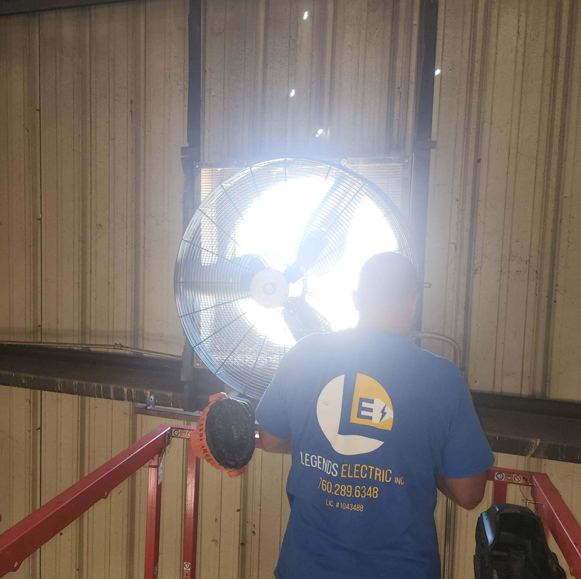 A man in a blue shirt is holding a fan in front of a window