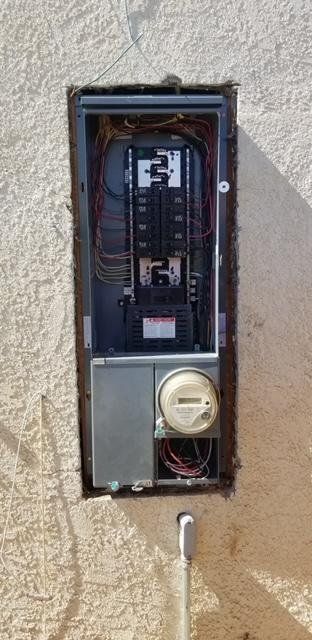 A electrical box is sitting on a wall next to a meter.