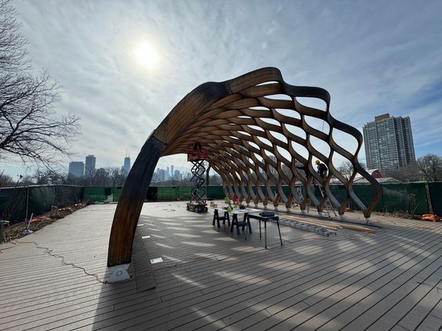 Wooden pavilion on a boardwalk, with city skyline in the background under a sunny sky.