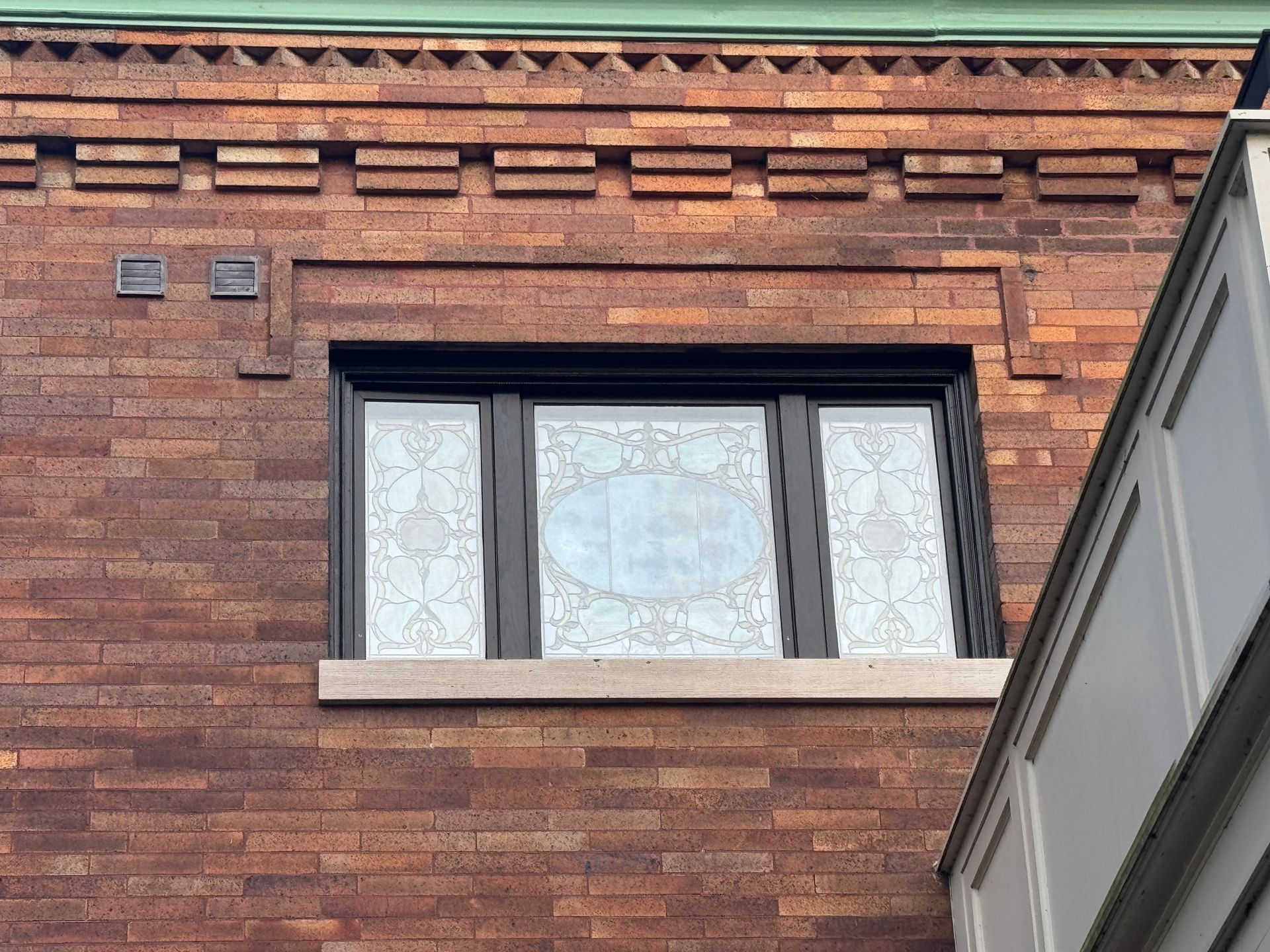 A brick building has a window with a stained glass design on it