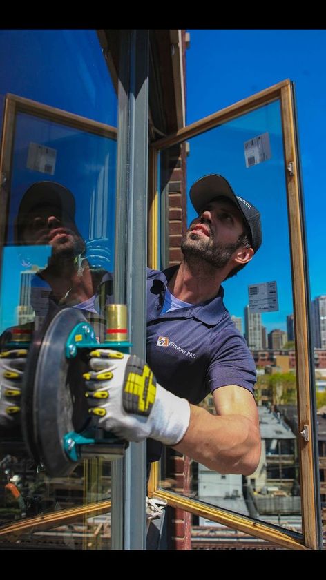 Man in cap, holding suction cup to install glass window, with cityscape in background.