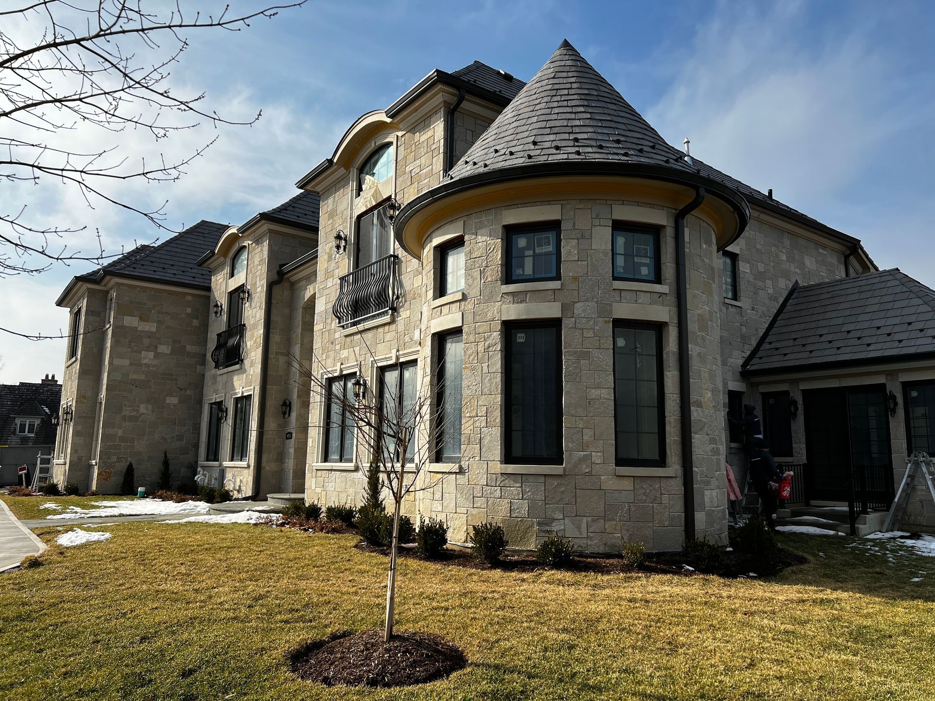 Large stone mansion with turret, dark roof, and green lawn on a sunny day.