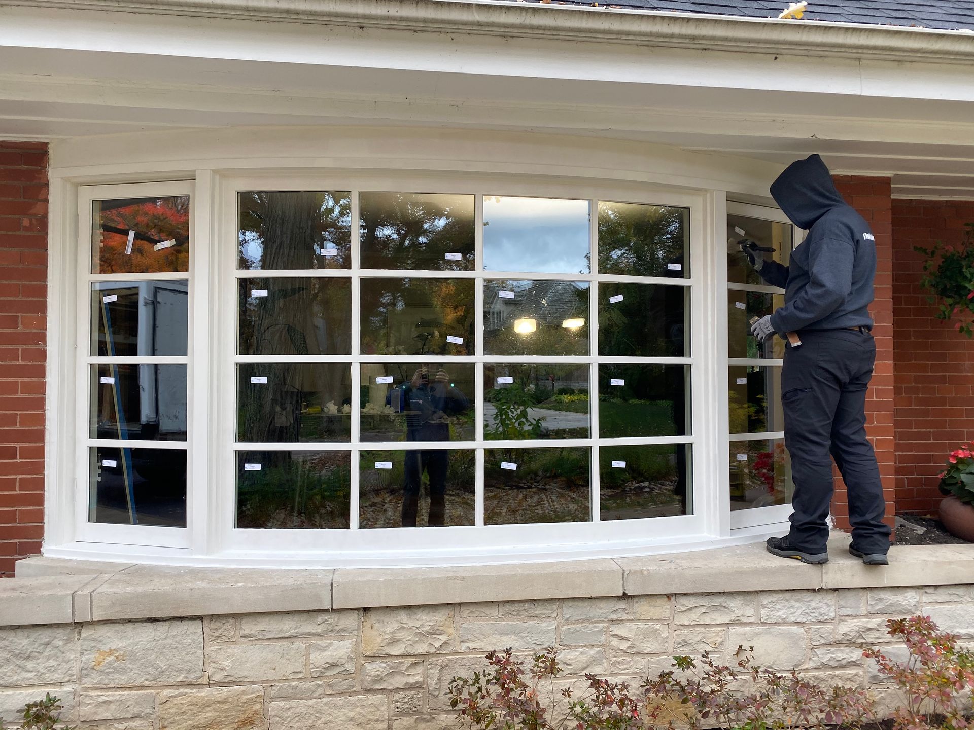 Person installing windows in a white-framed bay window on a brick house.