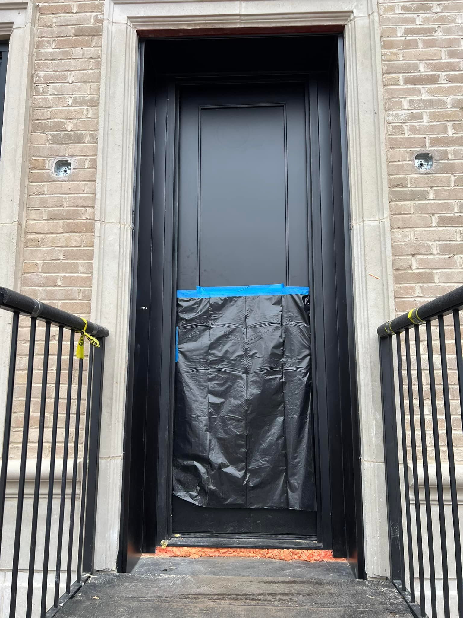 A black door is being painted on a brick building.