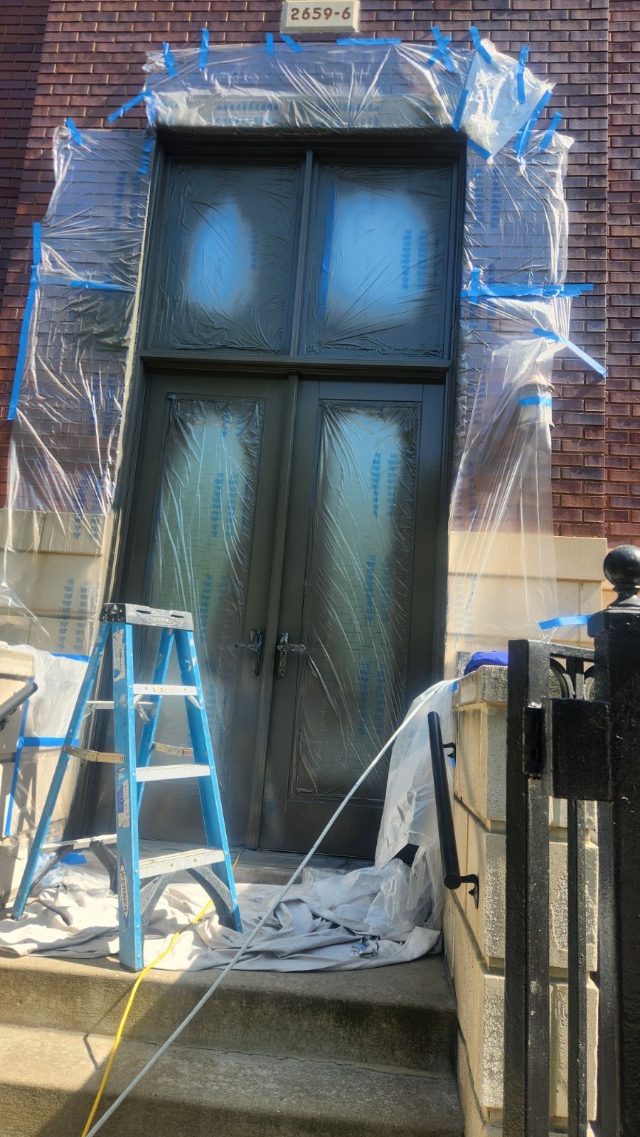 A door is being painted in front of a brick building.