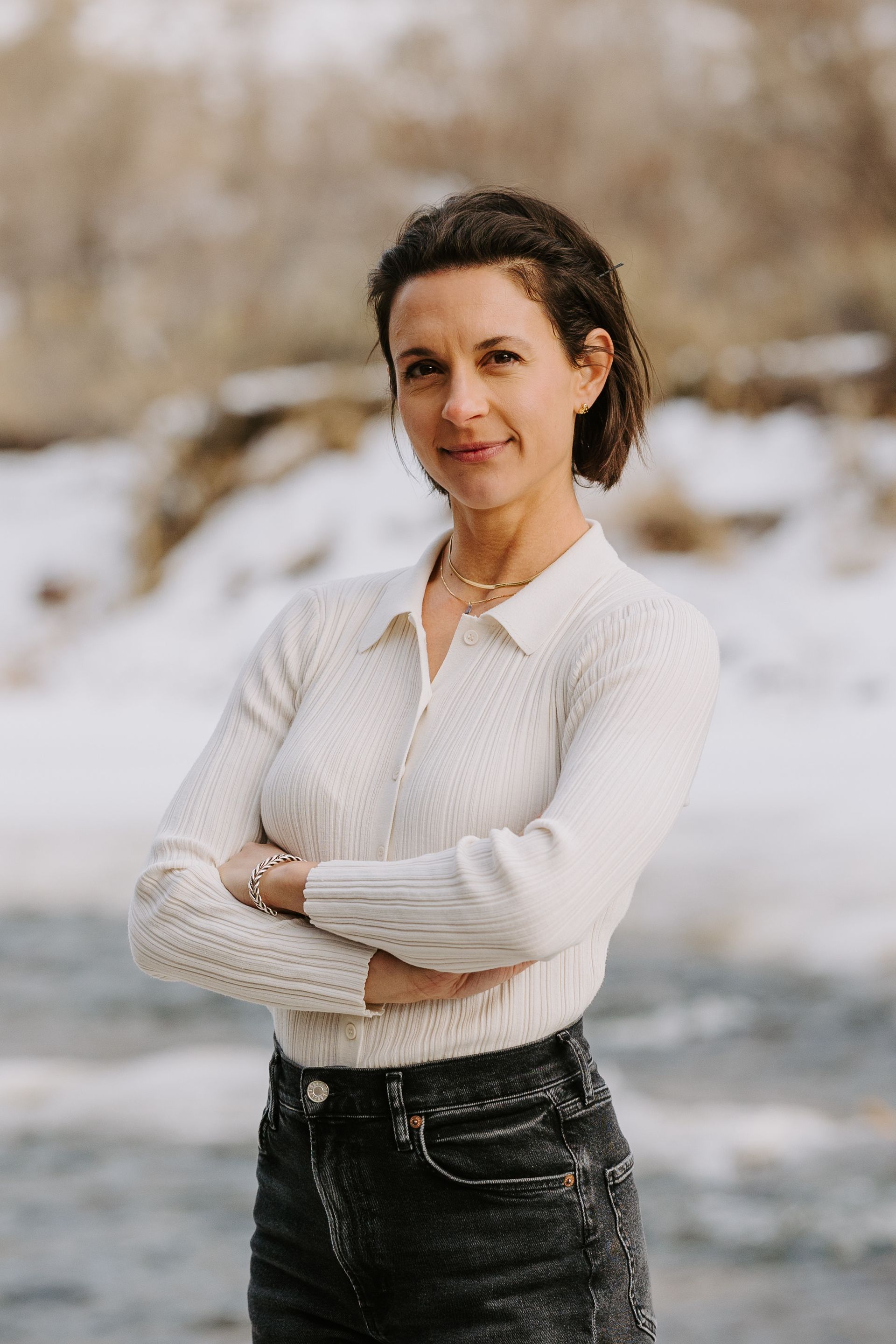 A woman is standing in the snow with her arms crossed.