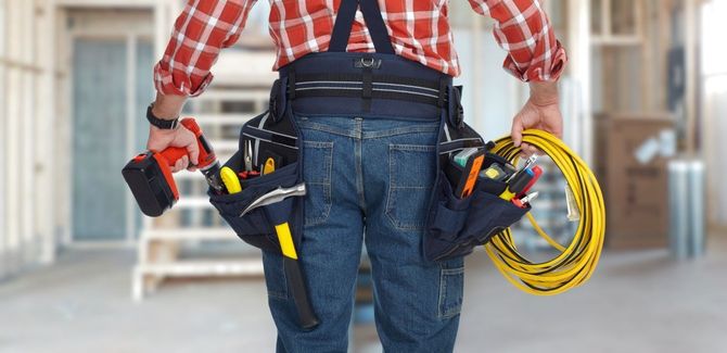 Construction worker in a plaid shirt carrying tools and a yellow cable reel