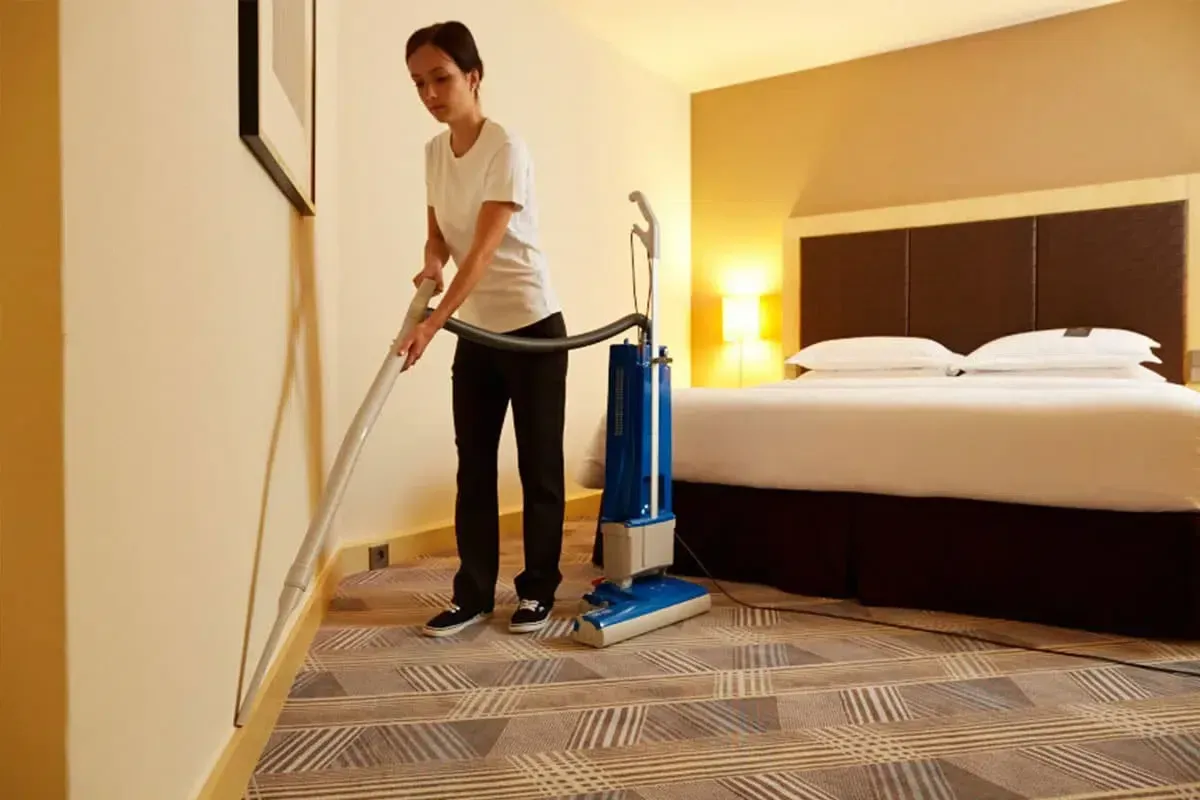 Eine Frau benutzt in einem Hotelzimmer einen Staubsauger.