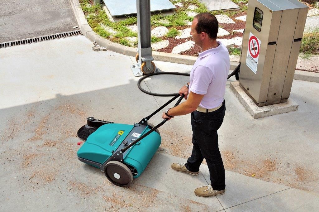 Ein Mann schiebt eine Kehrmaschine auf einer Betonfläche