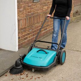 Eine Frau schiebt eine blaue Kehrmaschine auf einem Bürgersteig