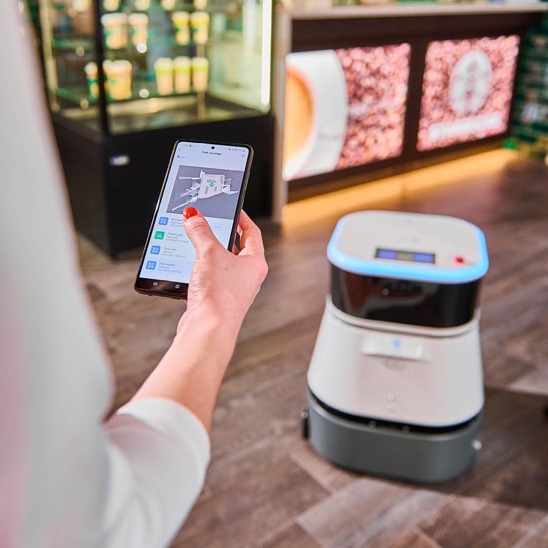 Eine Frau hält ein Mobiltelefon vor einen Roboter.